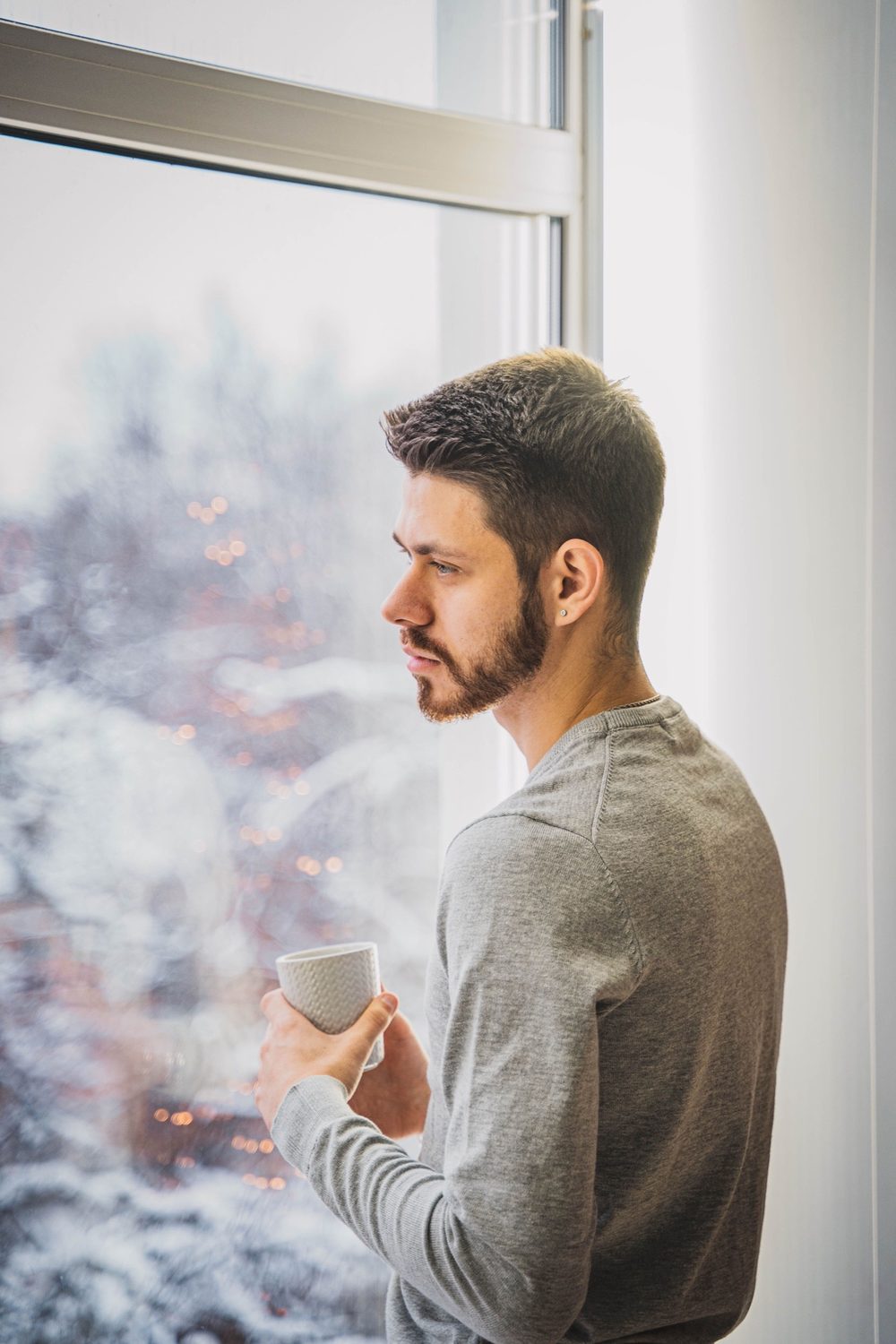 Man gazing out a window holding a mug, a quiet reflective moment
